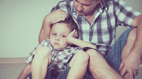 sad father with arm around sad-looking school-aged boy