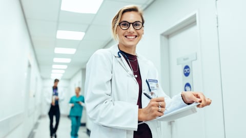 Young white blonde woman physician in a hallway smiling