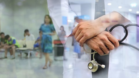 Close up of doctors folded hands holding a stethoscope with the blurry background of a hospital