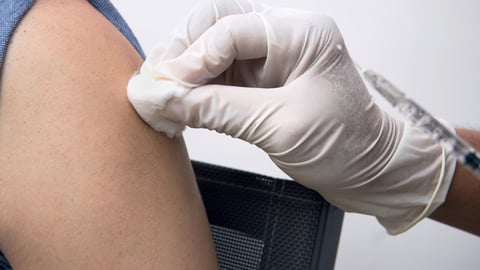 A healthcare provider swabs a shoulder before administering a vaccine. 