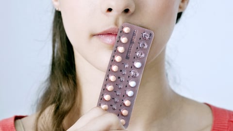 Young woman holding a packet of pills to her face