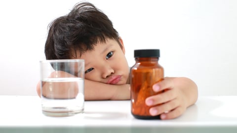 Young boy sadly contemplating a bottle of pills, uninterested in taking his medicine