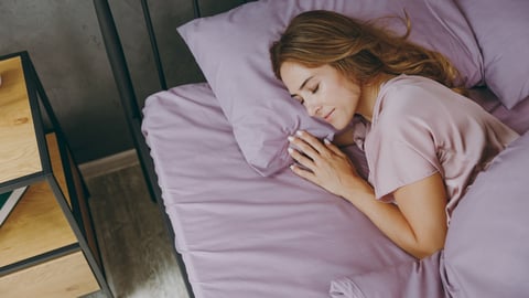 Middle aged woman sleeping in purple bedding