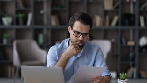 Young man working at laptop, looking at papers