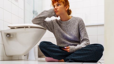 Young woman sitting beside a toilet on the floor looking despondent