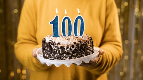 Woman holding birthday cake with number 100 candle, close up.