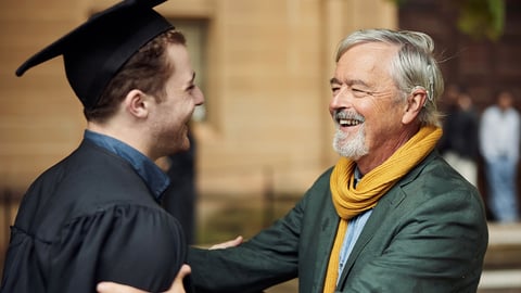 A man in a graduation gown shakes hands with another man