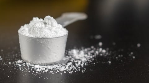 Creatine powder in a measuring scoop, pre-workout for gym on black wooden background.