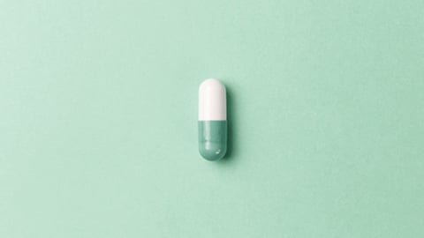 A single green and white capsule pill on a green background