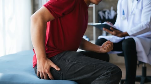Young man sitting on a doctor's exam table holding his haunch in pain