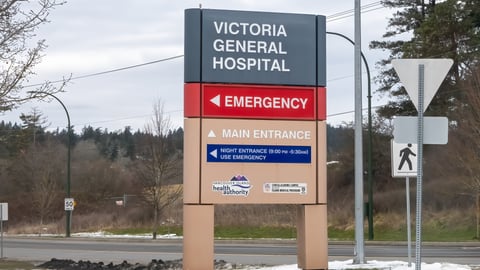 Victoria General Hospital's exterior signage under an overcast sky directs patients to the Emergency and Main Entrance, including after-hours instructions.