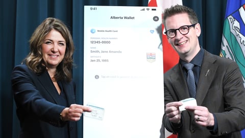 Alberta Premier Danielle Smith and Technology and Innovation Minister Nate Glubish hold up their old health cards during an announcement for the new digital health cards. (Government of Alberta)