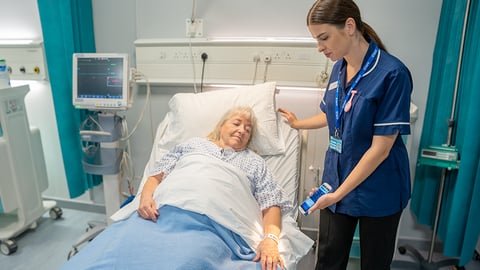 Nurse caring for a patient in hospital bed.