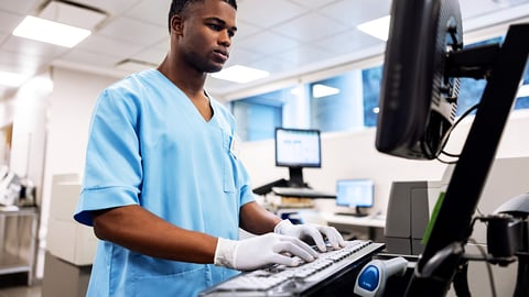 Healthcare worker in scrubs typing on keyboard.