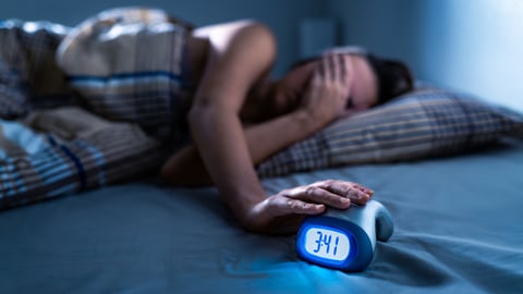 Young woman holding her hand over her eyes, distressed by not being able to sleep