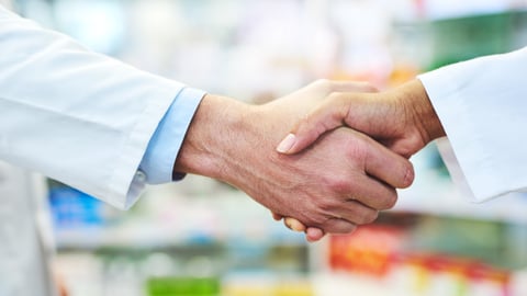 Two pharmacists shake hands at a pharmacy.