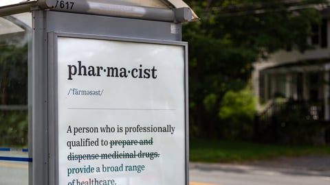 A bus stop with an ad with the new definition of "pharmacist"