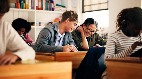 Two teenagers smitten with each other sharing a joke in a classroom