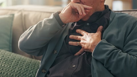 Close up of an older man holding his chest because he's having trouble breathing