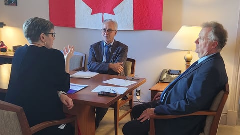 Dr. Carolyn Flegg Dr. Julian Dobranowski and MP Kevin Waugh discuss around a table under a quilted Canadian flag