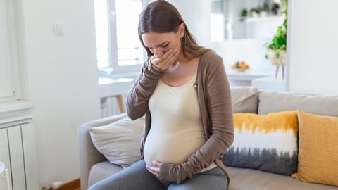 A nauseated pregnant woman sitting on a bed trying not to throw up
