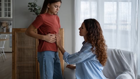 Young teen girl gripping her side, telling her mother she is having pain