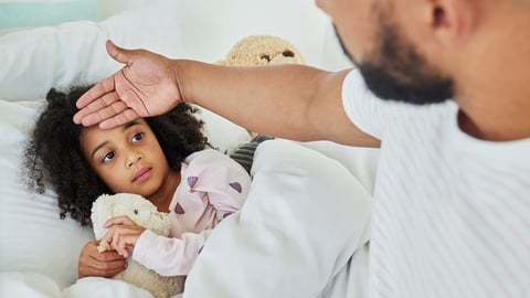 Young girl in bed with a fever as her father checks her temperature with the back of his hand