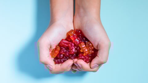 Fair-skinned child's cupped hands full of red gummy vitamins