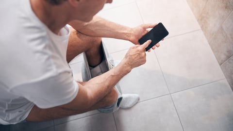 overview of white guy sitting on toilet scrolling on smartphone