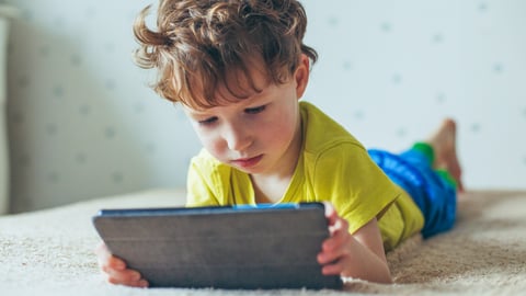 A young boy watching a tablet while laying on his stomach