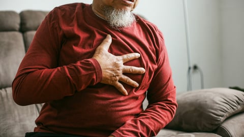 Older man in a red shirt clutching his chest in pain