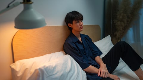 lonely young Asian man sitting on bed , looking sad