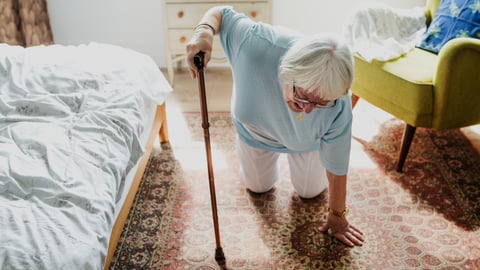 Elderly woman, white, white hair, by bed, on knees, has fallen, holding cane