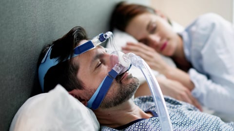 Young white man in bed with partner, wearing a sleep apnea mask