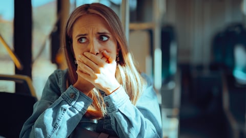Young woman riding on the bus covering her mouth with her hands because she's afraid she might vomit