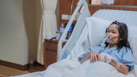 Young east Asian girl in a hospital bed with a respiratory mask