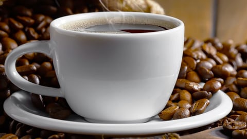 coffee in white porcelain cup sitting on a blanket of coffee beans.