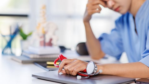 A doctor holds her head in stress while holding a stethoscope. 