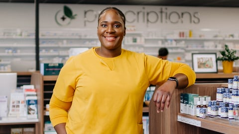 A young Black woman pharmacist in a bright yellow sweater in her pharmacy