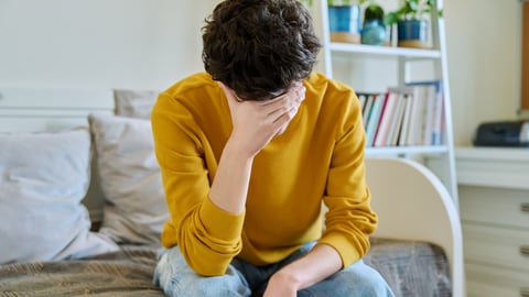 Sad upset young man sitting on couch at home, touching his head with hands