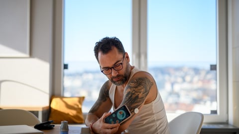 Tatooed white man checking his blood sugar with a continuous glucose monitor
