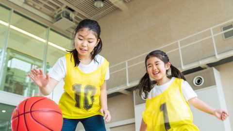 Two young Asian girls playing basketball with yellow jerseys