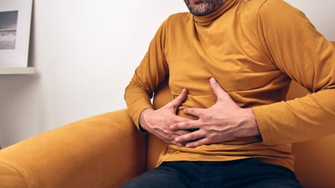 Man in a yellow shirt holding his stomach in discomfort