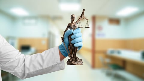 A medical professional wearing a white coat and blue gloves holding a statue of Justice