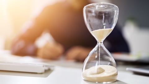 An hourglass on a desk in front of a man.