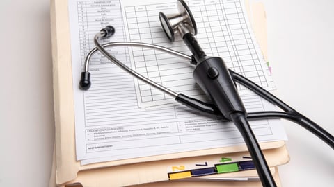 A stack of medical records underneath a stethoscope. 