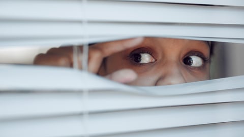 A young woman poking the blinds up so she can peek out the window