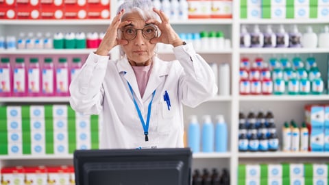 Older woman pharmacist holding her glasses to emphasize she is looking closely at something