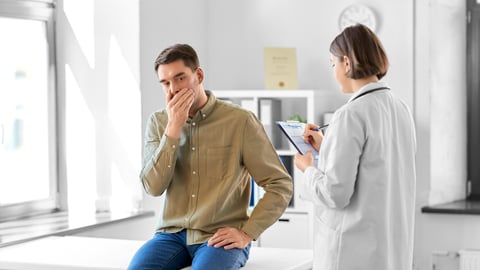 A patient covers his mouth in front of a doctor in a doctor's office.