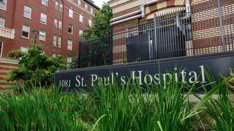  Paul's Hospital entrance sign showing St. Paul's Hospital mounted on dark fence with ornamental grasses in foreground